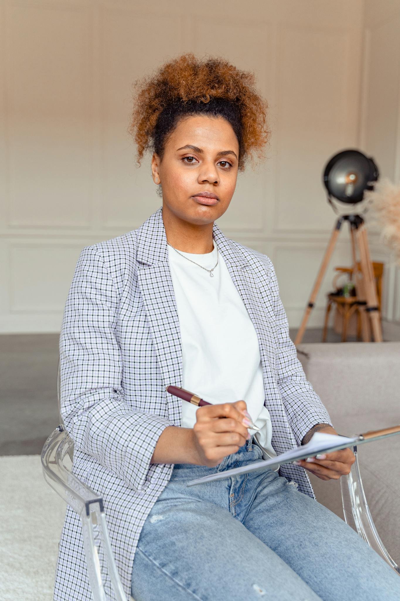 Serious woman in casual attire holding a clipboard in an office environment, suggesting a professional setting.
