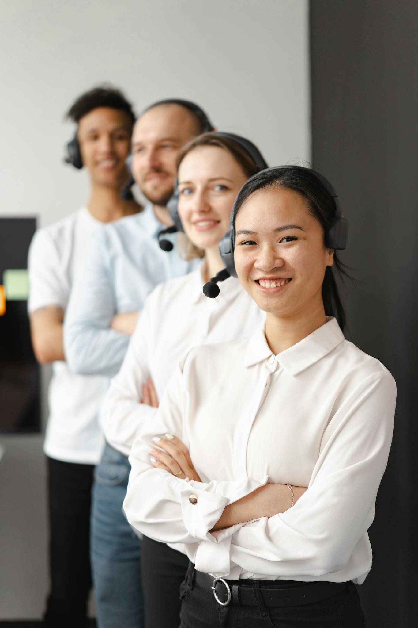 Smiling team of diverse call center agents with headsets, standing in line indoors.